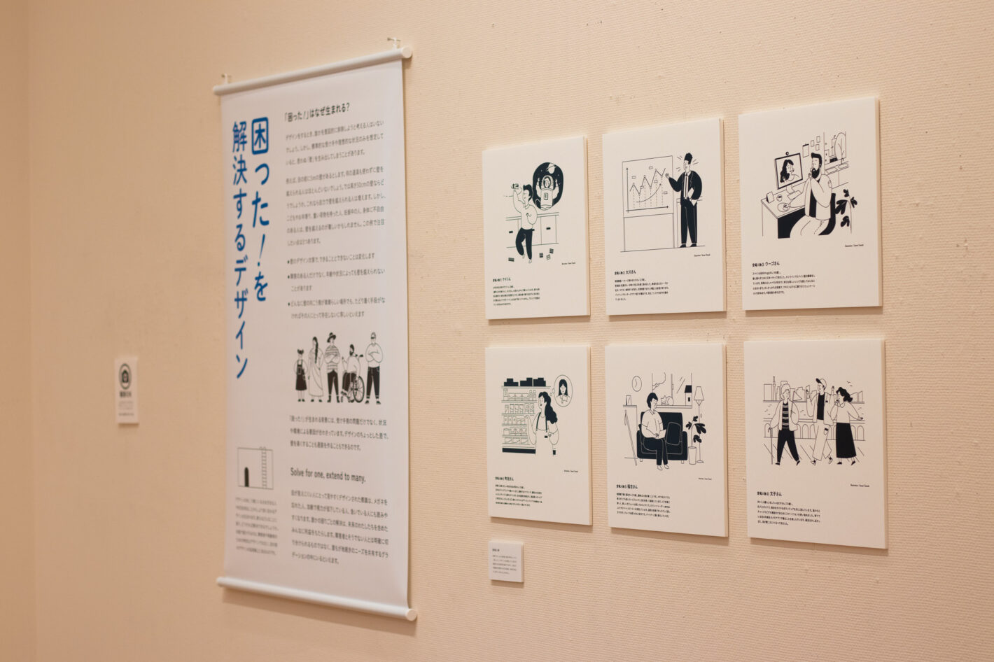 写真：「困った！を解決するデザイン」というタペストリーと、6人の登場人物のイラストとプロフィールが書かれたパネルの展示。