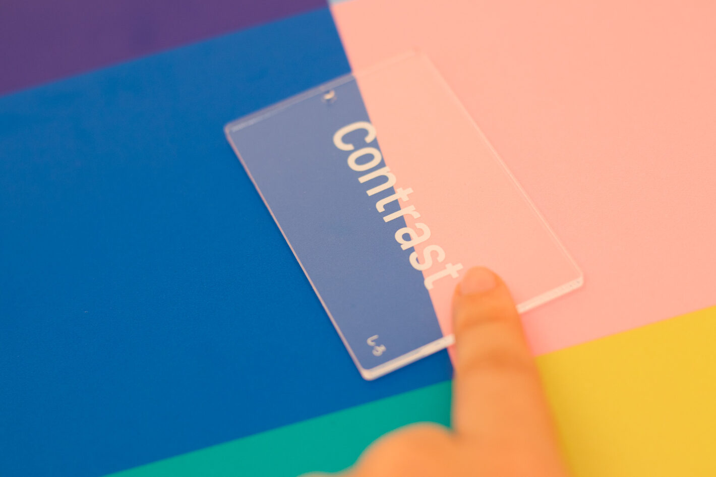 写真：白い文字のアクリルカードを、ピンク色と青の背景の間で動かしているところ。
