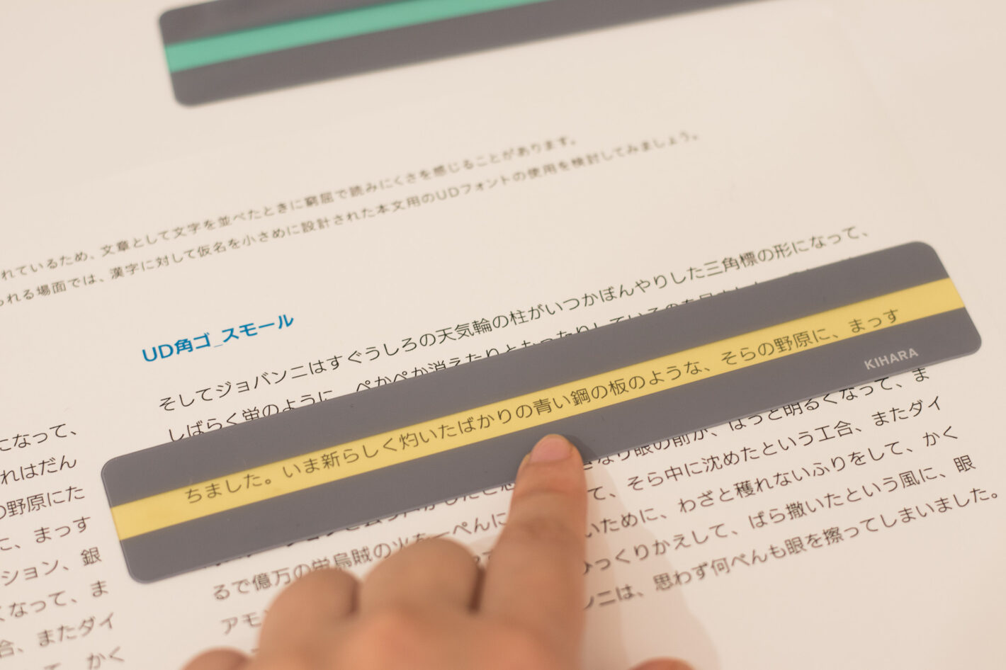 写真：UD角ゴ スモールで書かれた文章の上にイエローのリーディングトラッカーをあてています。リーディングトラッカーは定規のような形で、読んでいる1行をハイライトし、前後の行を隠す道具です。